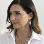 Model wearing a white shirt wearing diamond and sapphire earrings and a sapphire, diamond, and natural pearl necklace