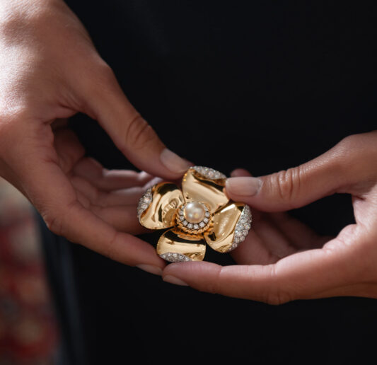 a pair of hands holding a gold, diamond, and pearl flower head brooch